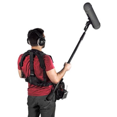 Man with a boom microphone wearing a harness and headphones for audio recording.